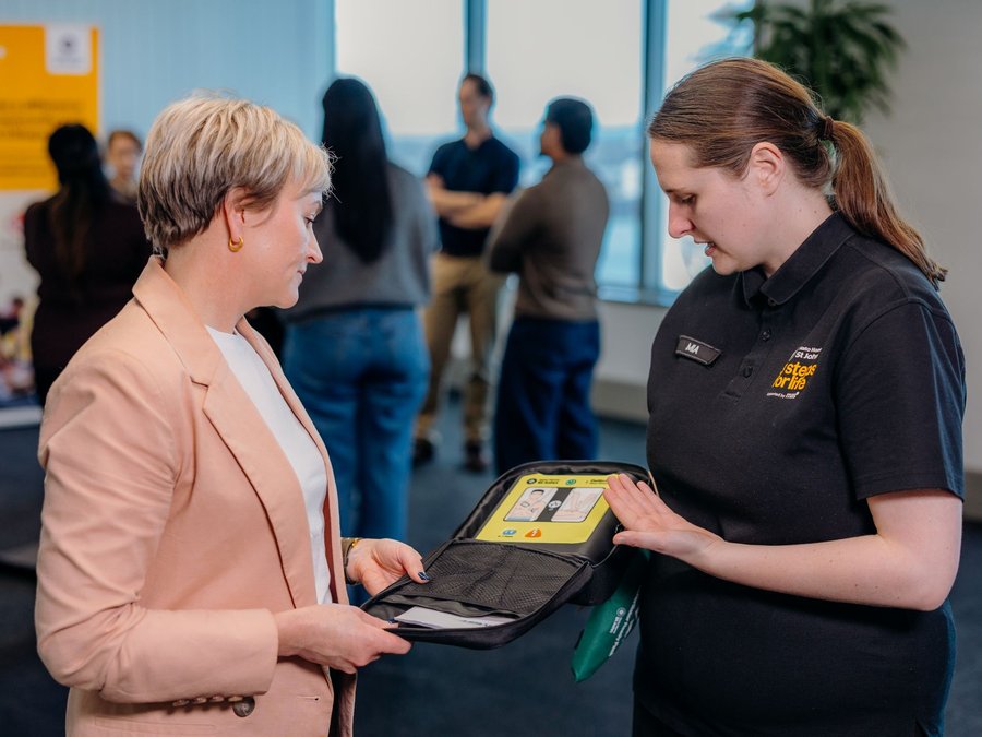3 Steps for Life instructor showing off a defibrillator to a woman in a nice jacket