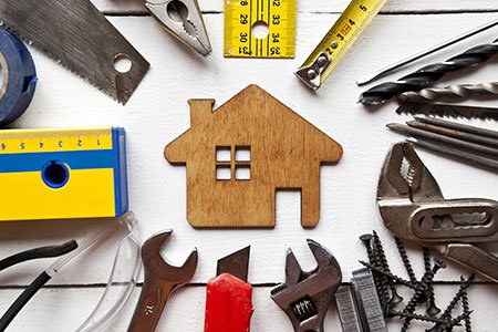 An array of tools on a wooden table with a wooden house in the middle