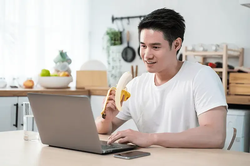 Asian business man eating healthy banana fruit while working from home.