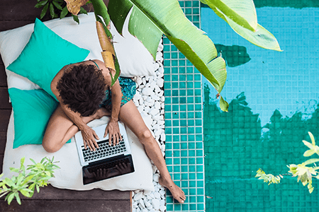 Birds eye view of a lady using her laptop outside next to a swimming pool