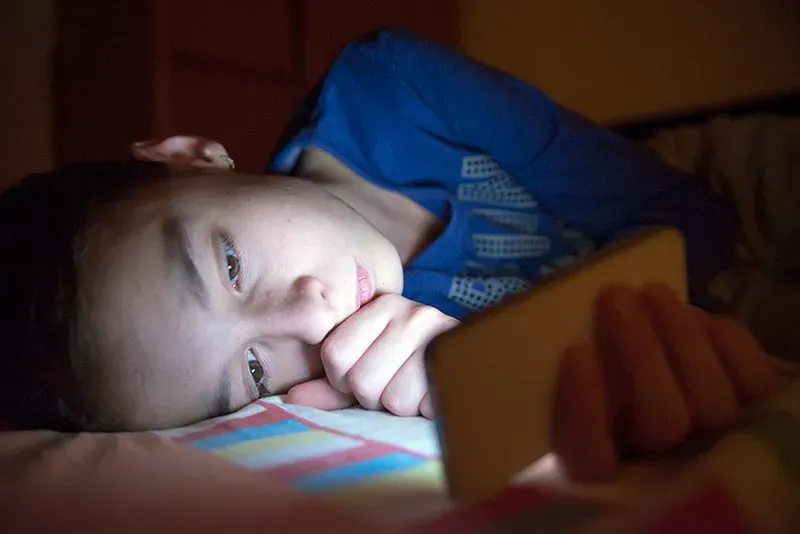 Boy laying down in bed reading his smartphone