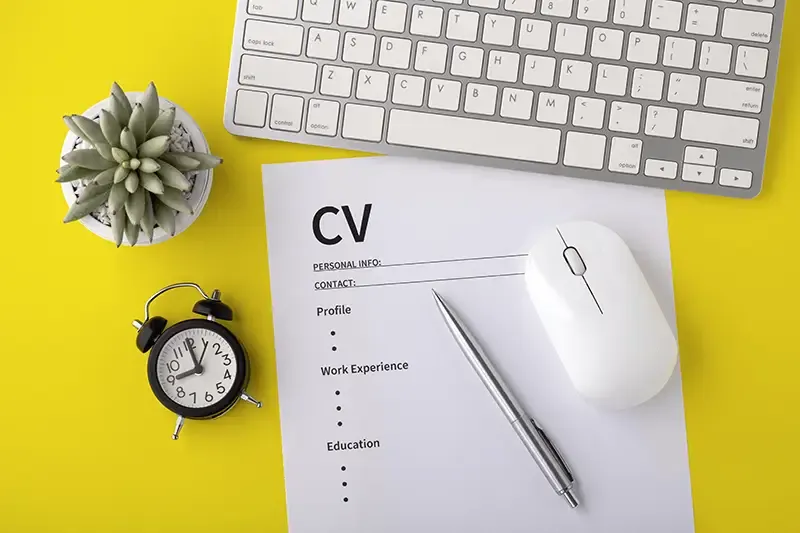 CV template next to a laptop, clock, pot plant and pen on a yellow background
