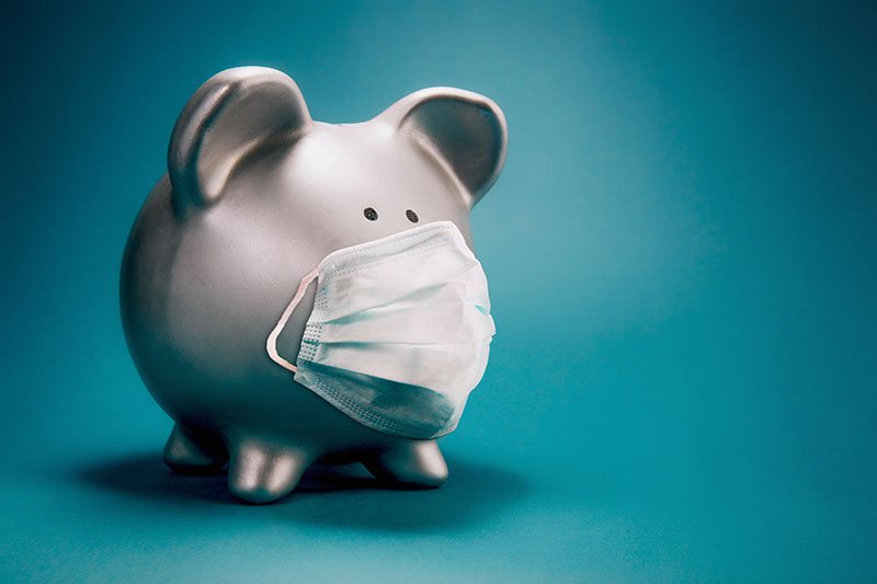 Close up of piggy bank, wearing protective face mask and isolated on blue background