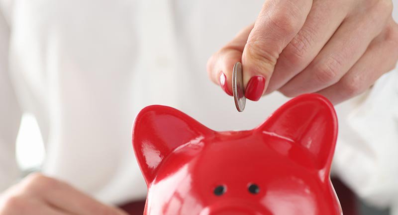 Close up of woman&#39;s hand putting a coin into a piggy bank