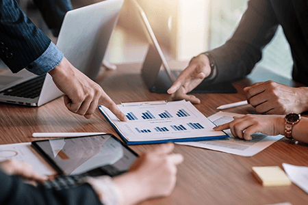 Close-up-view-of-business-people-investment-advisors-pointing-at-graph-and-analyzing-financial-report-in-meeting-listing.png