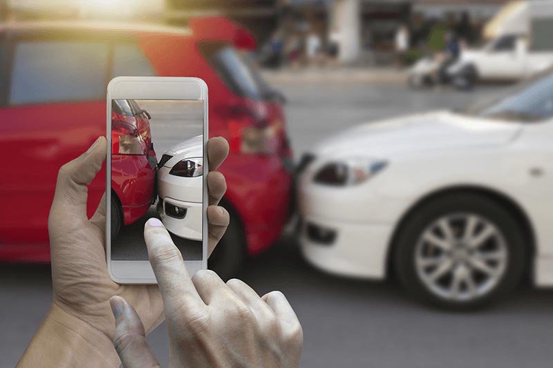 Close up of hand holding smartphone and taking a photo at the scene of a car crash