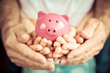 Adult and child hands holding a piggy bank together