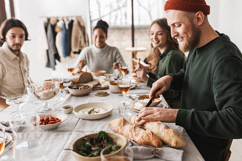 Group of friends sitting around a table eating dinner together smiling