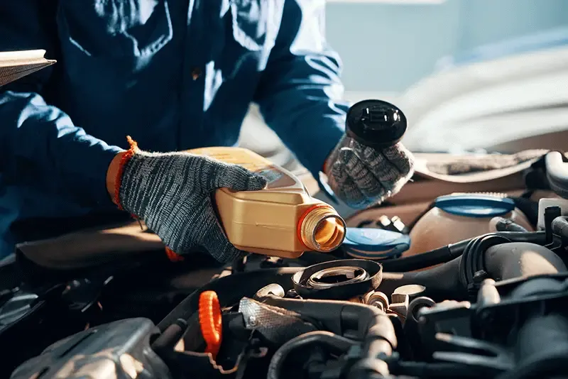 Gloved hands of a mechanic pouring oil into car engine