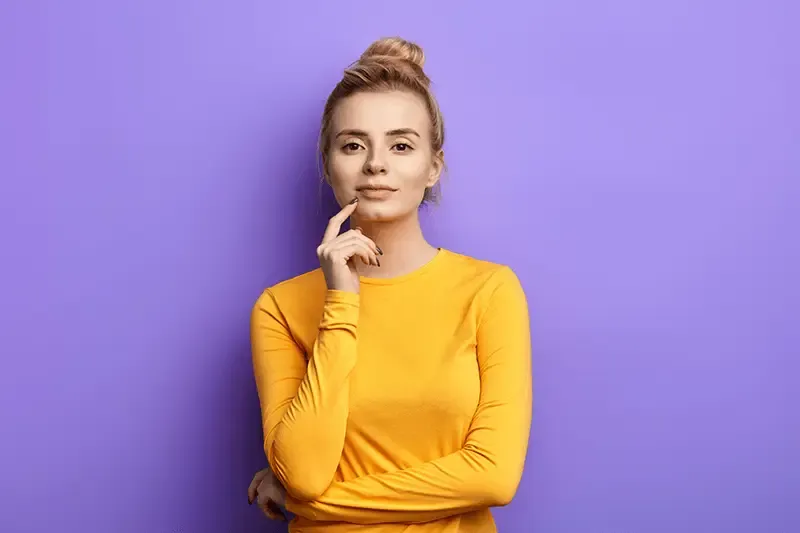 Good looking woman with her arm crossed and finger on chin smiling with purple background