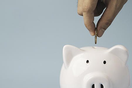 Hand putting coin to white piggy bank saving on blue background