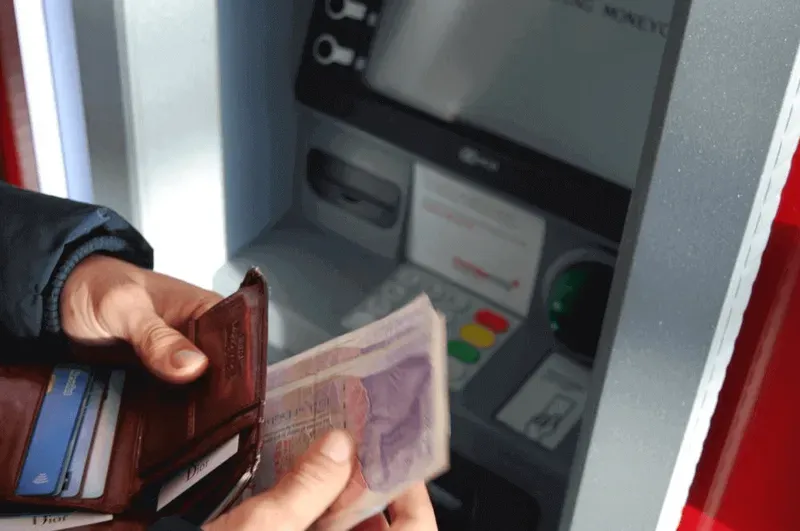 Hand holding wallet with bank notes in it in front of atm