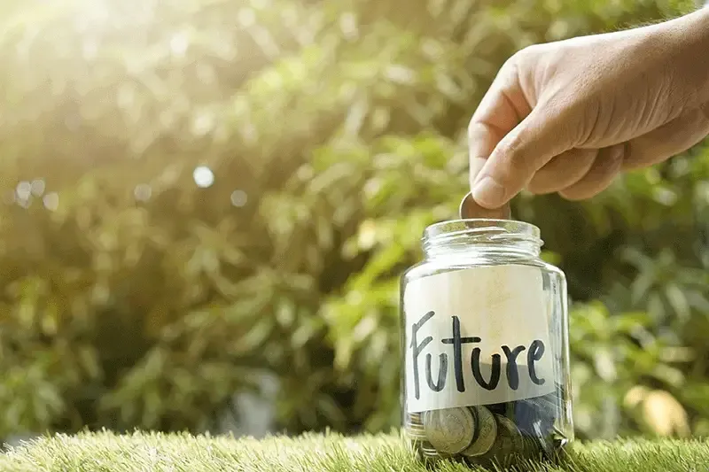 Hand putting a coin in a glass jar half filled with coins and the label &#39;future&#39; on it