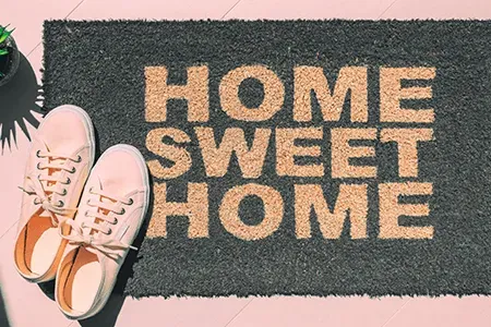Home sweet home doormat next to a pair of pink sneakers and houseplant
