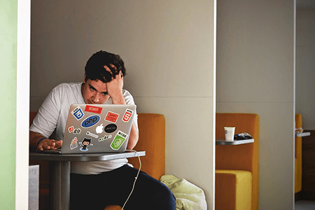 Stressed-man-sitting-in-a-booth-staring-at-a-laptop