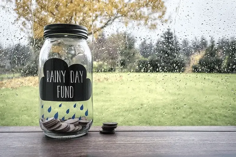 Jar on a window sill half full of coins with label &#39;rainy day fund&#39;