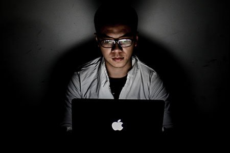 Man sitting in a dark room using his macbook