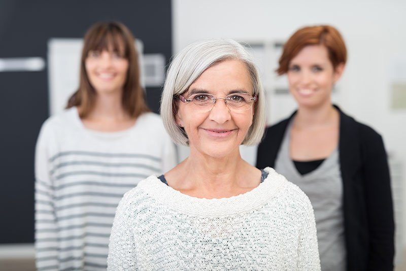 Older woman smiling at the camera with two younger women smiling behind her