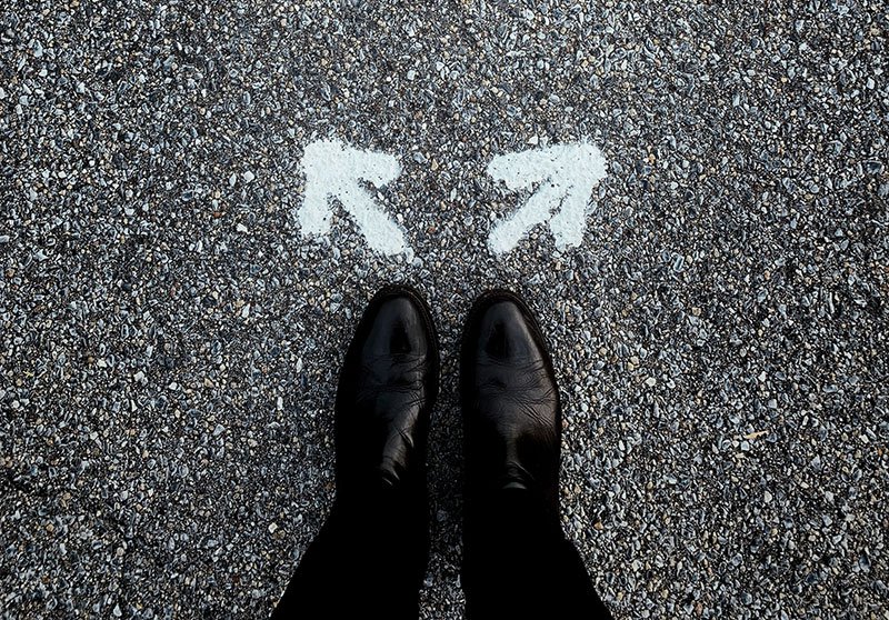 A pair of feet standing behind two white arrows leading in different directions