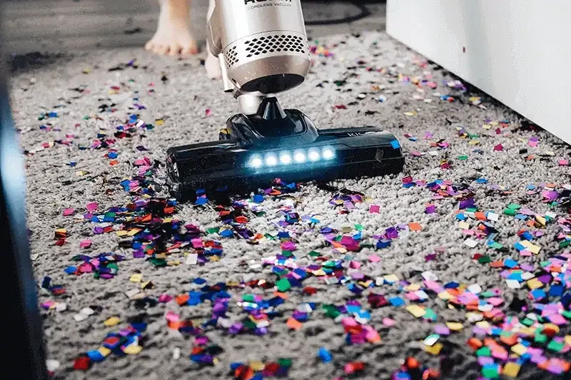Person vacuuming confetti from a dark grey rug