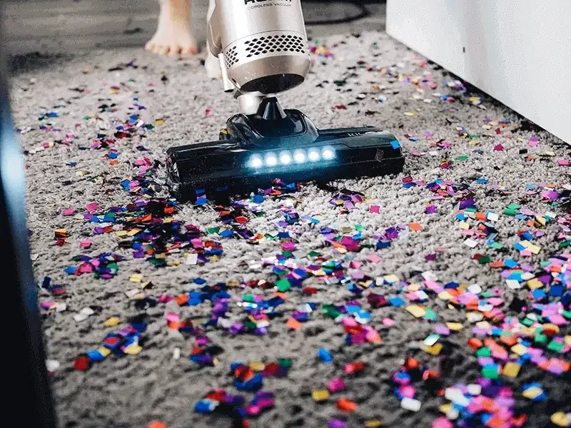 Person vacuuming confetti from a dark coloured rug