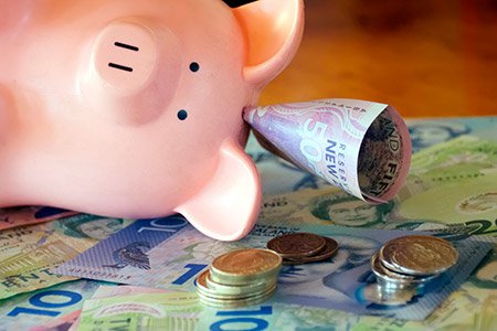 Piggy bank resting on a pile of New Zealand money