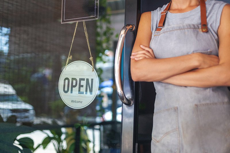 Small business owner stands next to open sign