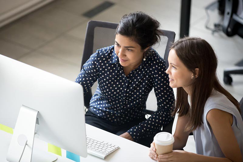 Two colleagues looking at laptop screen together in office