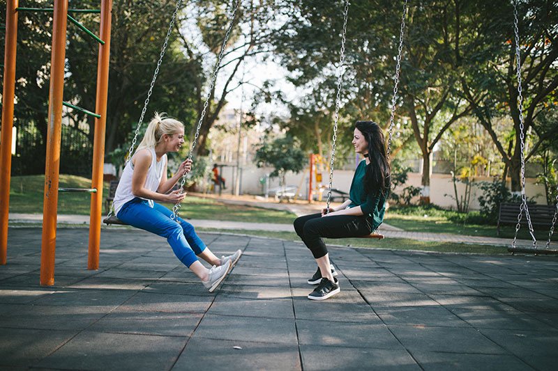 Two female friends sitting on a swing talking