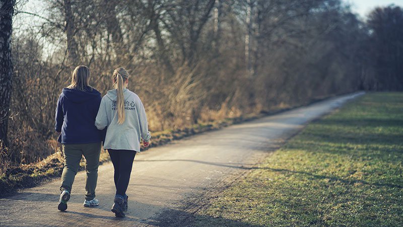 Two female friends walking together on footpath