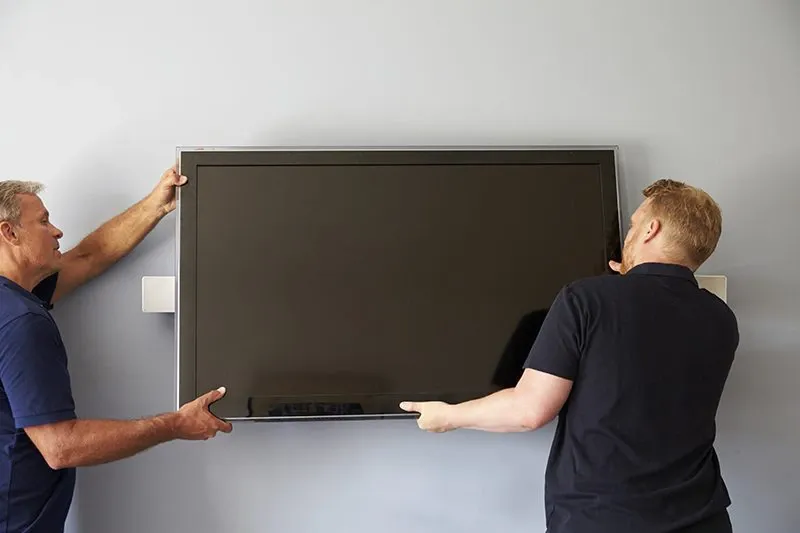 Two men fitting TV to wall mount in a home