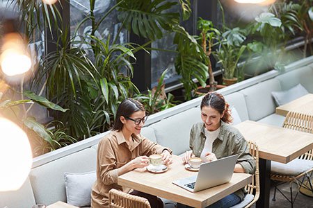 Two women sitting in an outdoor terrace drinking tea and looking at a laptop