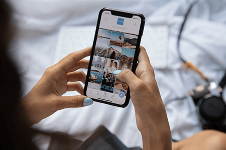 woman sitting on her bed looking at photos on her iphone
