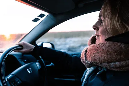 Woman wearing a jacket and scarf and driving a car during the daytime in winter