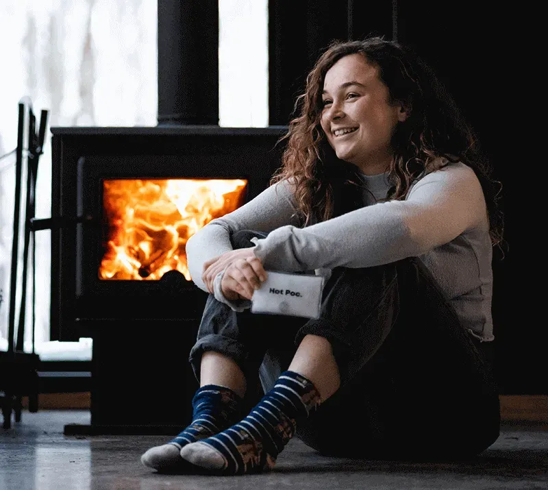 Woman sitting on floor next to a lit fireplace smiling