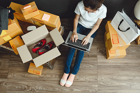 Women-sitting-on-laptop-surrounded-by-opened-and-unopened-boxes-of-online-purchases-listing.gif