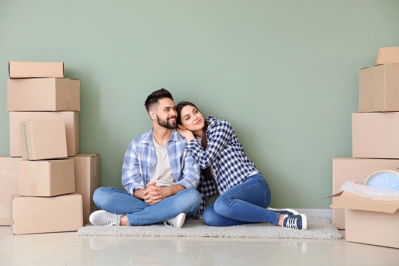 Young couple with belongings sitting near color wall in their new house