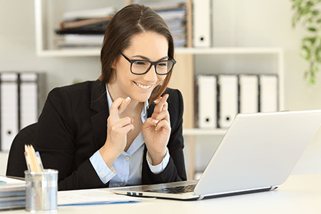 Young lady looking at laptop screen excitedly with fingers crossed