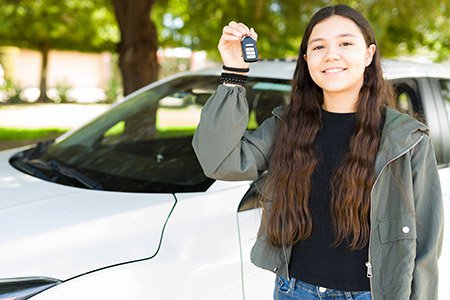 Young person next to first car holding keys