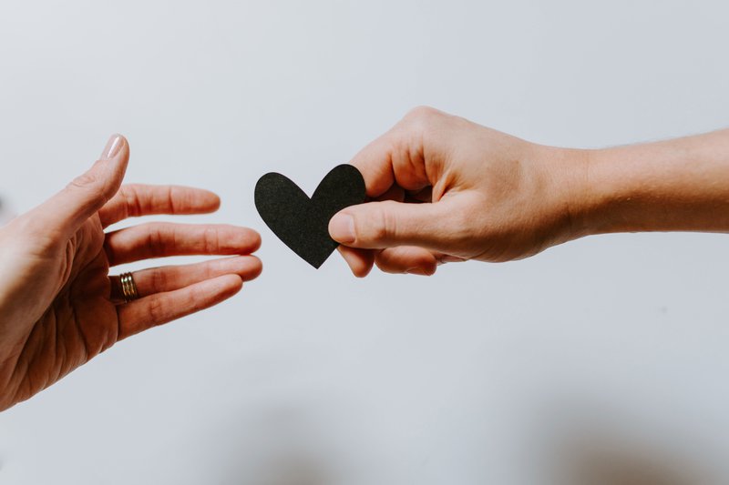 A hand reaching out to receive a black paper heart from another hand