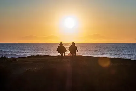 an elderly retired couple sitting on a beach watching the sun set listing.webp