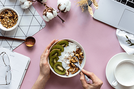 bowl of cereal surrounded by laptop glasses and a cup