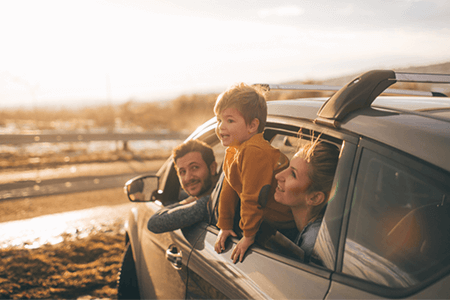 family-in-car-on-the-beach-with-little-kid-hanging-his-head-out-the-window