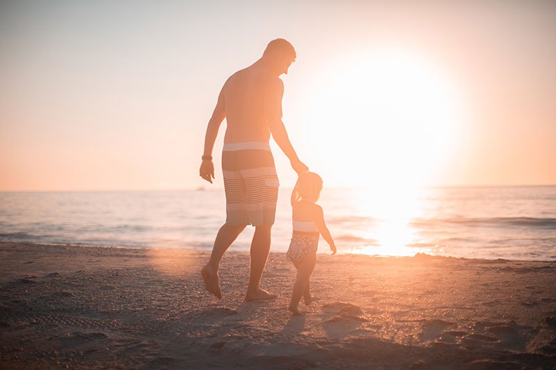 father and daughter walking hand in hand towards the ocean