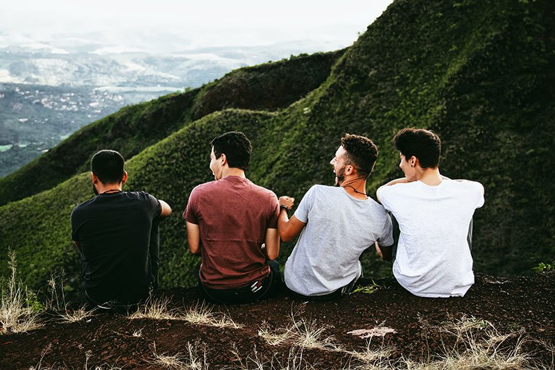 four male friends sitting together on a mountain laughing and smiling