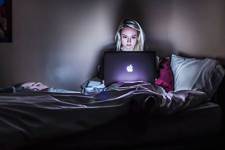 girl-on-macbook-on-bed-in-the-dark