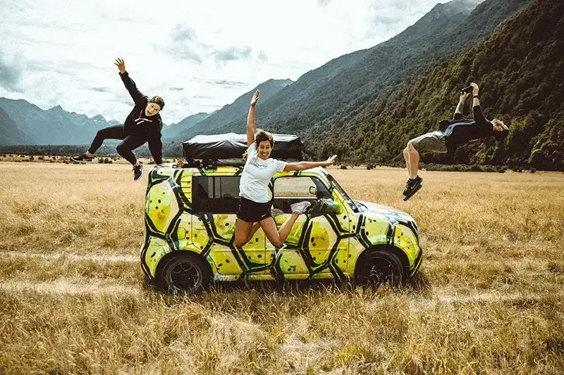 group of young people jumping excitedly in the air outside their rental car with a new zealand mountainside backdrop