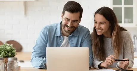 happy couple sitting at kitchen table looking at laptop screen