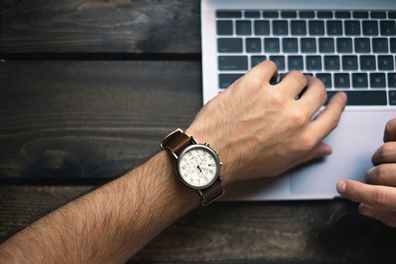 Male looking at his watch on his wrist while using a computer