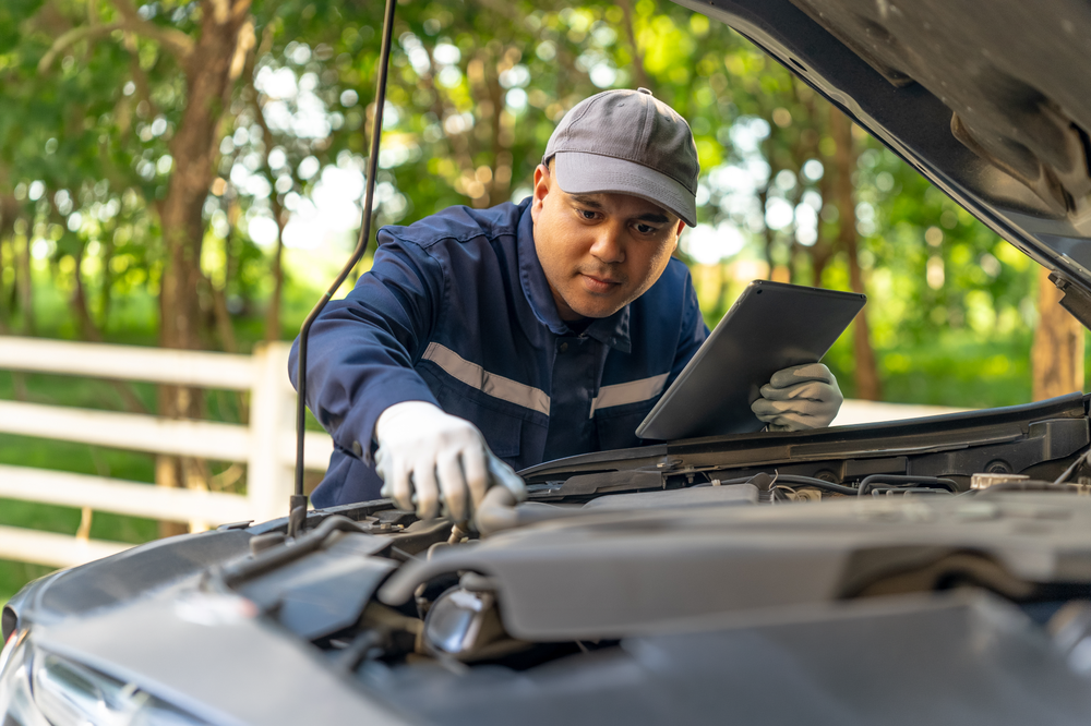 man assessing a car engine holding a tablet